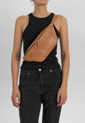 Kraftig læder sling taske med et diagonalt design, der har en top lynlås og et lille logo. Båret over kroppen.