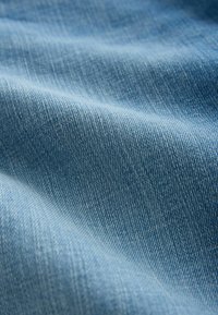 Zbliżenie na jasnoniebieską, teksturowaną tkaninę dżinsową z widocznym wzorem splotu i miękkimi fałdami tworzącymi delikatne cienie.