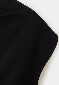 Gros plan sur la partie supérieure d'un vêtement noir sans manches sur fond blanc montrant la texture du tissu et les détails des coutures.