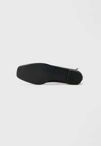Suola nera di scarpa con una finitura liscia, forma rettangolare e texture in gomma. Presenta un lieve tacco e un modello di battistrada minimo per la presa.