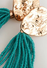 Türkise Perlenfransen mit glänzenden, goldmetallischen ovalen Akzenten, die eine strukturierte Oberfläche und ein hängendes Design aufweisen.