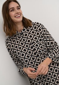 Long-sleeve button-up shirt featuring a black and cream geometric pattern with squares, black buttons, and a chest pocket. Soft, lightweight fabric.