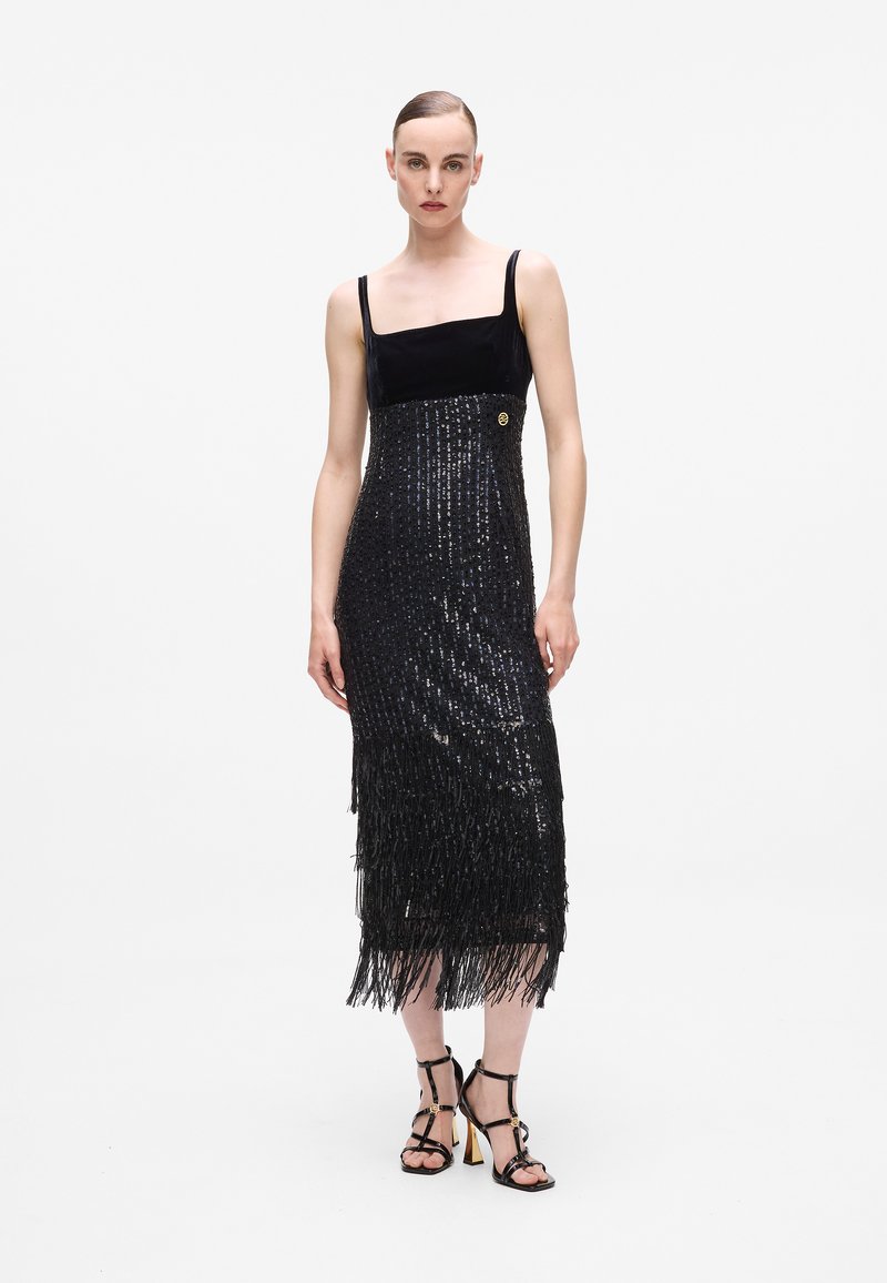 Črna obleka s sequinsom, ki ima prilegajoči sametni bodice, franje na robu in okrasno zlato gumb ob strani.