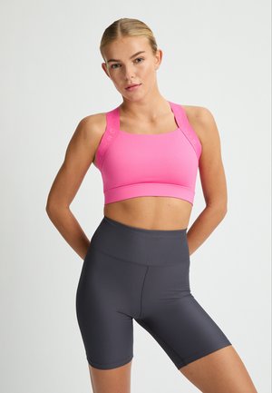 Pink sports bra with textured straps, paired with dark gray ribbed high-waist shorts. Both garments feature a snug fit for athletic use.