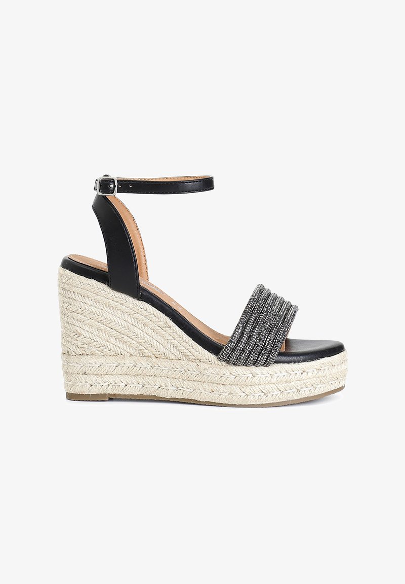 Musta nahkainen nousujalkapanta, jossa on tekstiilikoriste, espadrille-kuitu välipohja ja nilkkahihna. Neliön muotoinen varvasosa, litteä pohja.