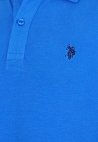 Modrá polo košile vyrobená z bavlny, s tříknoflíkovou légou a malým vyšitým logem jezdce na koni na levé hrudi.