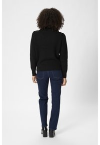 Schwarzer Strickpullover mit hohem Kragen, kombiniert mit dunkelblauen Jeans. Das Outfit zeichnet sich durch eine lockere Passform und eine glatte Textur aus. Schwarze, klobige Stiefel mit Absatz.