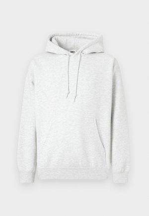 Svetlo siva kapuca iz mekog pamuka. Ima kengurudžersku džep, podesivu vezicu za kapu i rebarcaste manžete. Minimalno brendiranje.