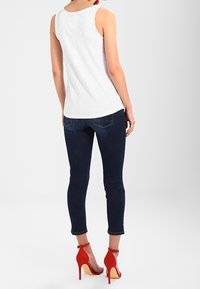 Witte mouwloze top met een aansluitend ontwerp, gecombineerd met donkerblauwe skinny jeans en rode hoge hakken, met enkelbandjes en open achterkant.
