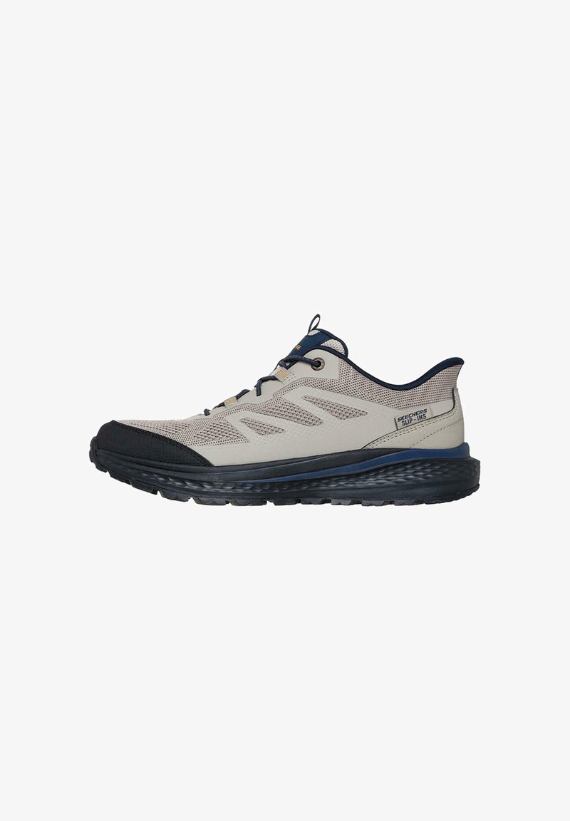 Zapato deportivo ligero con parte superior de malla y sintético. Color: beige y marino. Tiene una suela negra gruesa y patrones llamativos en el costado.
