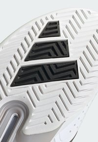 Suela de zapatilla deportiva blanca con patrones texturizados y tres acentos de goma negra en forma triangular. Diseñada para ofrecer tracción y durabilidad.
