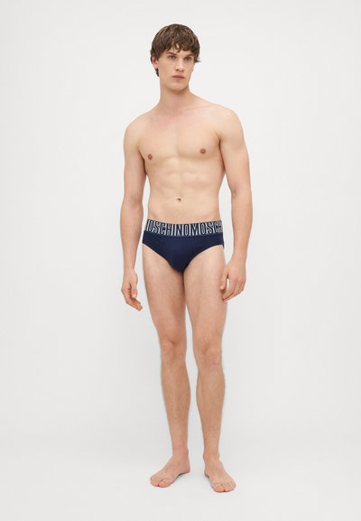 Fatos de banho para homem em azul-marinho, feitos de tecido elástico, apresentando uma cintura elástica contrastante com o logótipo "Moschino" em branco.