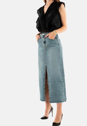 Falda maxi de mezclilla en lavado claro con abertura frontal, combinada con una blusa negra con detalles de encaje y un corte relajado. Tacones altos negros.
