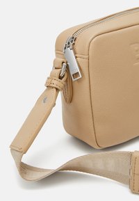 Tan läder crossbody-väska med rektangulär form, silverdragkedja och metallbeslag, med en slät yta och justerbar tygrem.