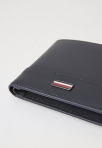 Navy leather wallet with a smooth texture, featuring a silver and colored striped accent and contrasting stitching. Compact and rectangular shape.