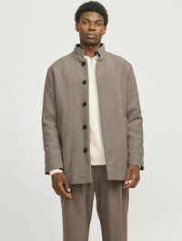 Grå uldfrakke med høj krave, designet med en lige skæring, prydet med sorte knapper og sidelommer. Båret over en lys sweater.