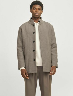 Manteau en laine gris avec un col haut, conçu avec une coupe droite, doté de boutons noirs et de poches latérales. Porté par-dessus un pull léger.