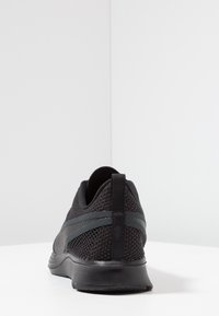 Chaussure de sport noire avec une tige en mesh, semelle en caoutchouc et un panneau arrière texturé. Présente une languette pour un enfilage facile et des accents de design subtils.