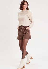 Beige strikket sweater med rund hals og diamantmønster; brune kordfløjl shorts med båndbelte; hvide hælede ankelstøvler.