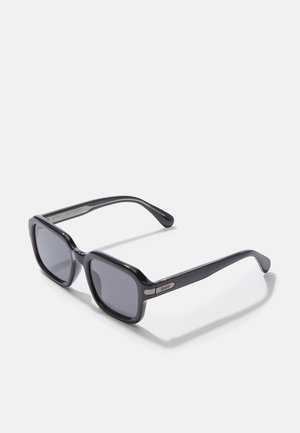 Occhiali da sole neri rettangolari con lenti scure, montatura in plastica spessa e dettagli in metallo argentato sulle tempie. Bracci con texture per una migliore presa.