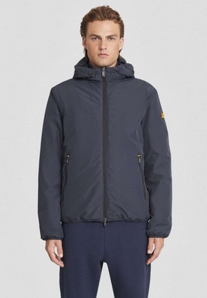 Giacca impermeabile blu navy con cappuccio, chiusura a zip, polsini elasticizzati, due tasche laterali e un piccolo logo sulla manica.