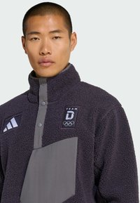 Polaire noire à col montant, accents gris et patchs logo sur la poitrine, avec boutons-pression et une poche avant.