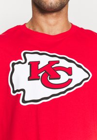 T-shirt en coton rouge avec un grand logo des Kansas City Chiefs en blanc contour noir et rouge. Design à col rond avec des manches courtes.