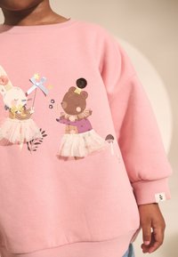 Felpa rosa con due personaggi animali illustrati in abiti da ballerina con accenti in tulle e decorazioni. Texture del materiale morbido.