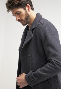 Palton din lână în gri închis, cu un design cu două rânduri de nasturi, butoane mari și rever cu crestătură. Textură netedă și croi ajustat.