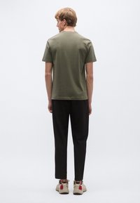 Olívazöld rövid ujjú póló, pamut anyagból, kerek nyakkivágással, fekete, szűk szárú nadrággal és piros részletekkel díszített bézs tornacipővel párosítva.