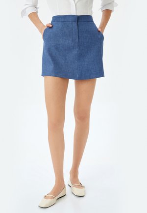 Mini gonna blu a trama con tasche laterali, caratterizzata da un taglio dritto e una cintura liscia, abbinata a scarpe bianche basse.