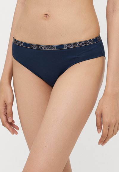 Tumedat sinised bikiinialused, millel on sile tekstuur ja mis on varustatud Emporio Armani bränditud elastse vöökohtaga. Klassikaline lühikese lõikega disain.