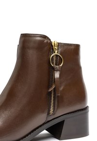 Stivale in pelle marrone alla caviglia con zip laterale, accessori in oro e tacco robusto. Texture liscia con una leggera lucentezza e design pulito e arrotondato.
