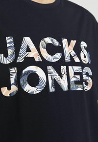 Jūrų tamsiai mėlynas marškinėliai su dideliu „JACK&JONES“ logo, išdėstyta gėlių raštais; trumpomis rankovėmis, apvaliu kaklu, pagaminti iš medvilnės, kasdieniškas dizainas.
