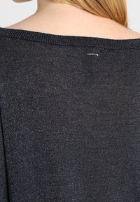 Ciemnoszary sweter dzianinowy o luźnym kroju i dekolcie odsłaniającym ramiona. Delikatny połysk materiału z małą metką marki widoczną z tyłu.