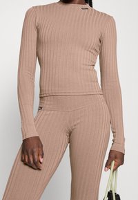 Prążkowany top z długim rękawem i dopasowane spodnie w jasnobrązowym materiale, z okrągłym dekoltem i subtelną metką z logo na ramieniu.