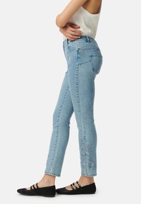 Jasnoniebieskie dżinsy skinny z kwiatowym haftem przy dolnej krawędzi. Posiadają wysoki stan i klasyczny krój z pięcioma kieszeniami.