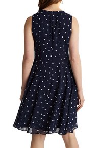 Marinblå klänning med vita prickar, ärmlös design, utsvängd kjol och dragkedja i ryggen. Lätt, mjukt tyg med en subtil lyster.
