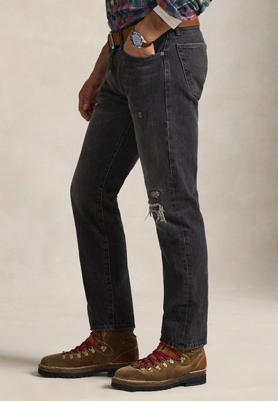 Μαύρο τζιν denim με λεπτομέρειες φθοράς, ίσια εφαρμογή, σχεδίαση με πέντε τσέπες και μεταλλικές λεπτομέρειες. Φορεμένο με καφέ μποτάκια πεζοπορίας.