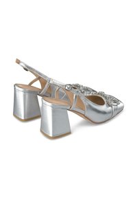 Scarpe col tacco alto in metallo argento con tacco quadrato spesso, apertura sul retro e cinturino decorativo con strass sulla parte anteriore.