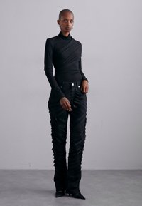Haut noir à manches longues avec un design torsadé associé à un pantalon noir côtelé présentant des plis verticaux. Le pantalon a une taille haute et une coupe slim.