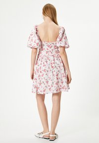Bloemendress met pofmouwen, witte stof met roze en groene bloemenpatronen, en een diepe ruglijn. Draag het met witte sandalen.