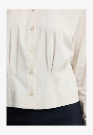 Cream blouse with five buttons, featuring pleats and a structured fit. Made from smooth fabric, it has a rounded hem and long sleeves.