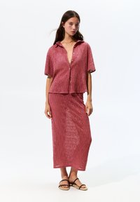 Dieprood, getextureerde twee-delige outfit met een kort knoopshirt en een lange, nauwsluitende rok, voorzien van een geometrisch patroon en een relaxte pasvorm.