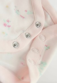 Puha rózsaszín baba ruha apró virágmintákkal, fém és textil patentokkal az élek mentén a rögzítéshez.