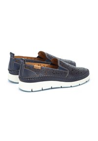 Zapatos de cuero azul marino sin cordones con patrones florales recortados, costura trenzada y una suela de goma blanca. Etiqueta de marca en el talón.