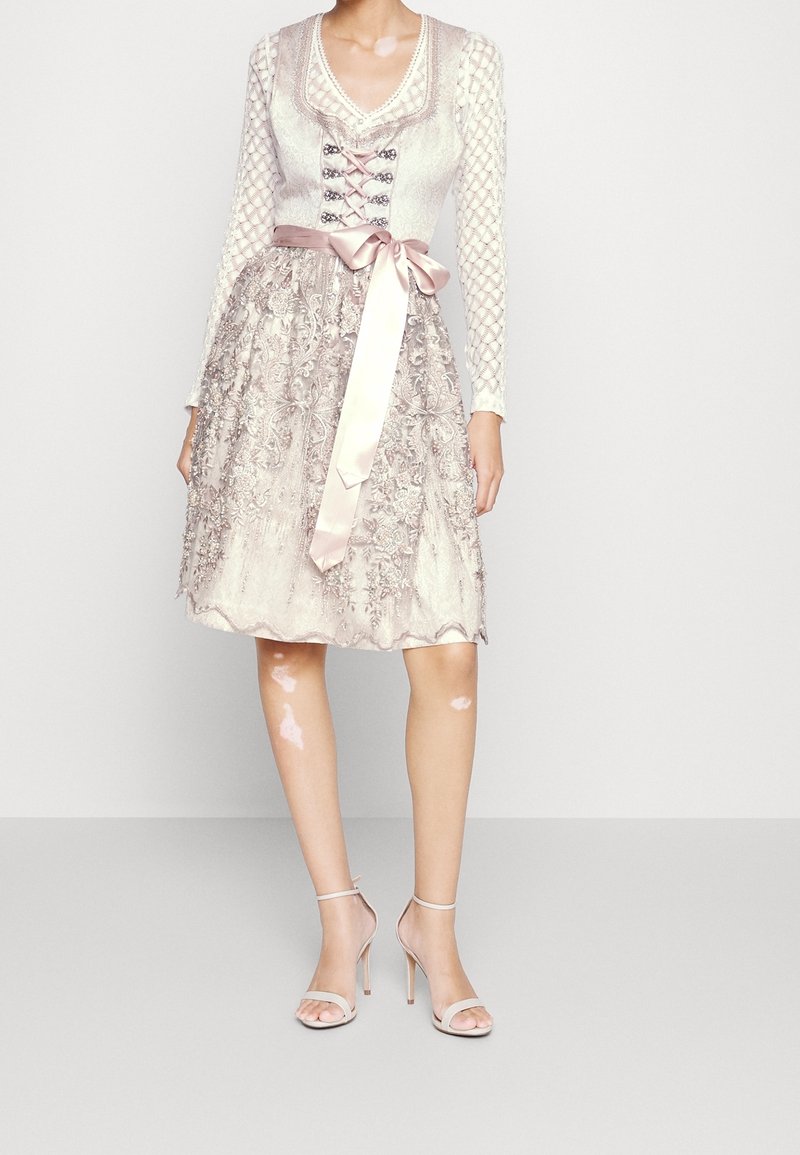 Robe en dentelle et satin de couleur beige doux, avec un corsage ajusté, un lien en ruban et une jupe brodée, dotée de manches longues et d'un ourlet évasé.