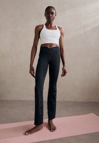 Fekete leggings és fehér crop top testhezálló kivitelben. A leggings magas derekú, sima textúrájú és enyhe szárszélesítéssel rendelkezik az alján.