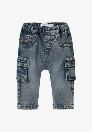 Gaiši zili džinsa bikses ar elastīgu jostu, sānu kabatām un vienu cargo kabatu uz kreisās kājas. Ar bojātu tekstūru visā virsmā.