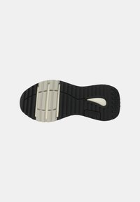 Suela de zapato con textura de goma negra, que presenta acentos blancos suaves, estrías y un logo. El diseño incluye patrones de agarre para tracción.